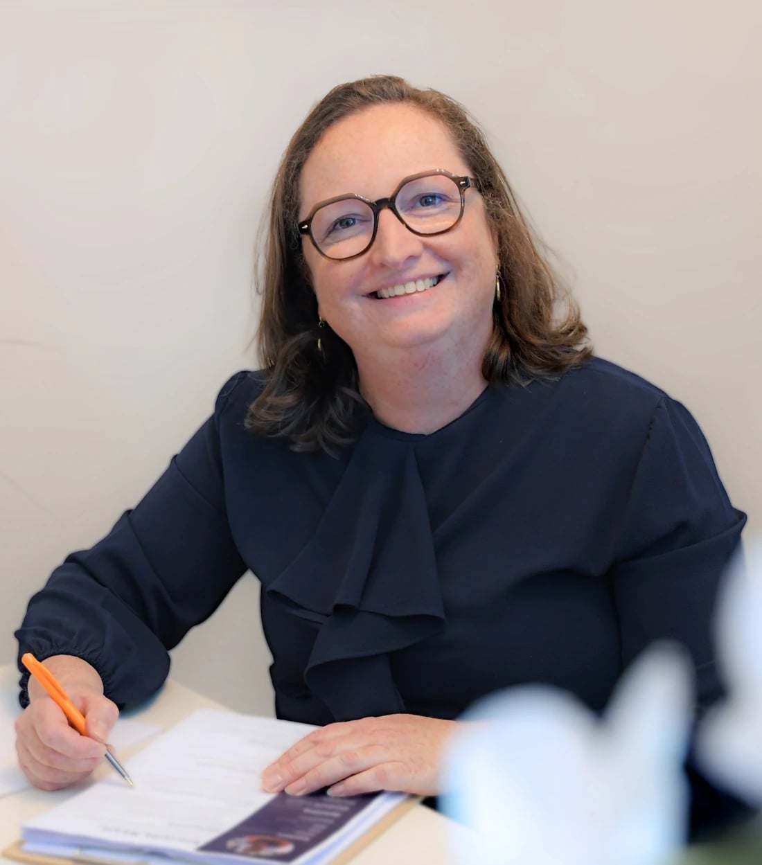 Elfriede Neels lacht aan haar bureau, met een pen in de hand