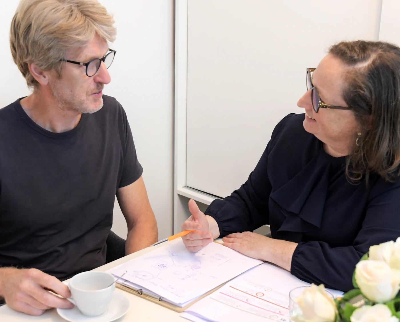 Elfriede Neels in gesprek met een cliënt aan tafel, met koffie en notities